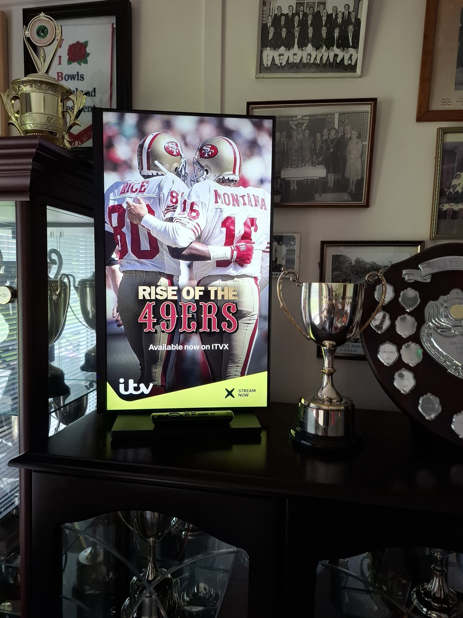 ITVX sports documentary campaign on a portrait Grassroot Media screen among trophies in a cricket clubhouse.