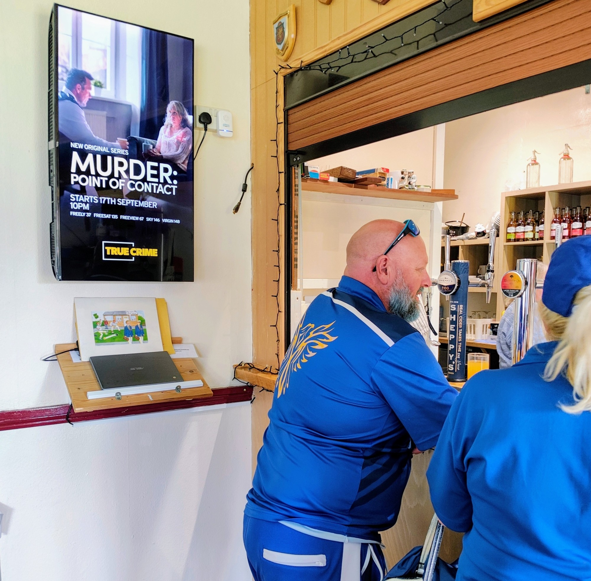 TRUE CRIME campaign on a wall-mounted portrait Grassroot Media screen beside the bar in a bowls clubhouse.