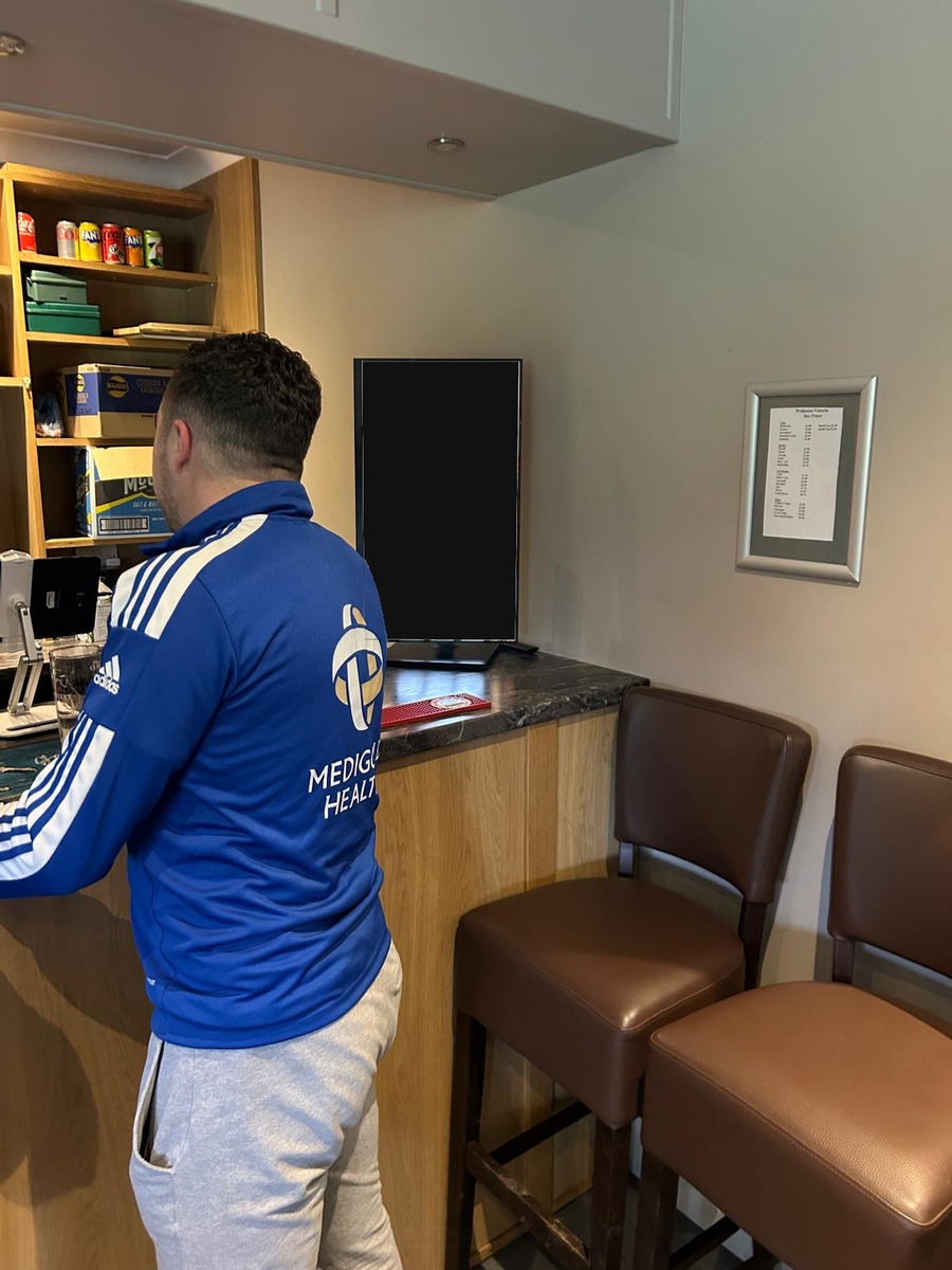 Grassroots football club bar showing the real clubhouse environment around a portrait digital screen.