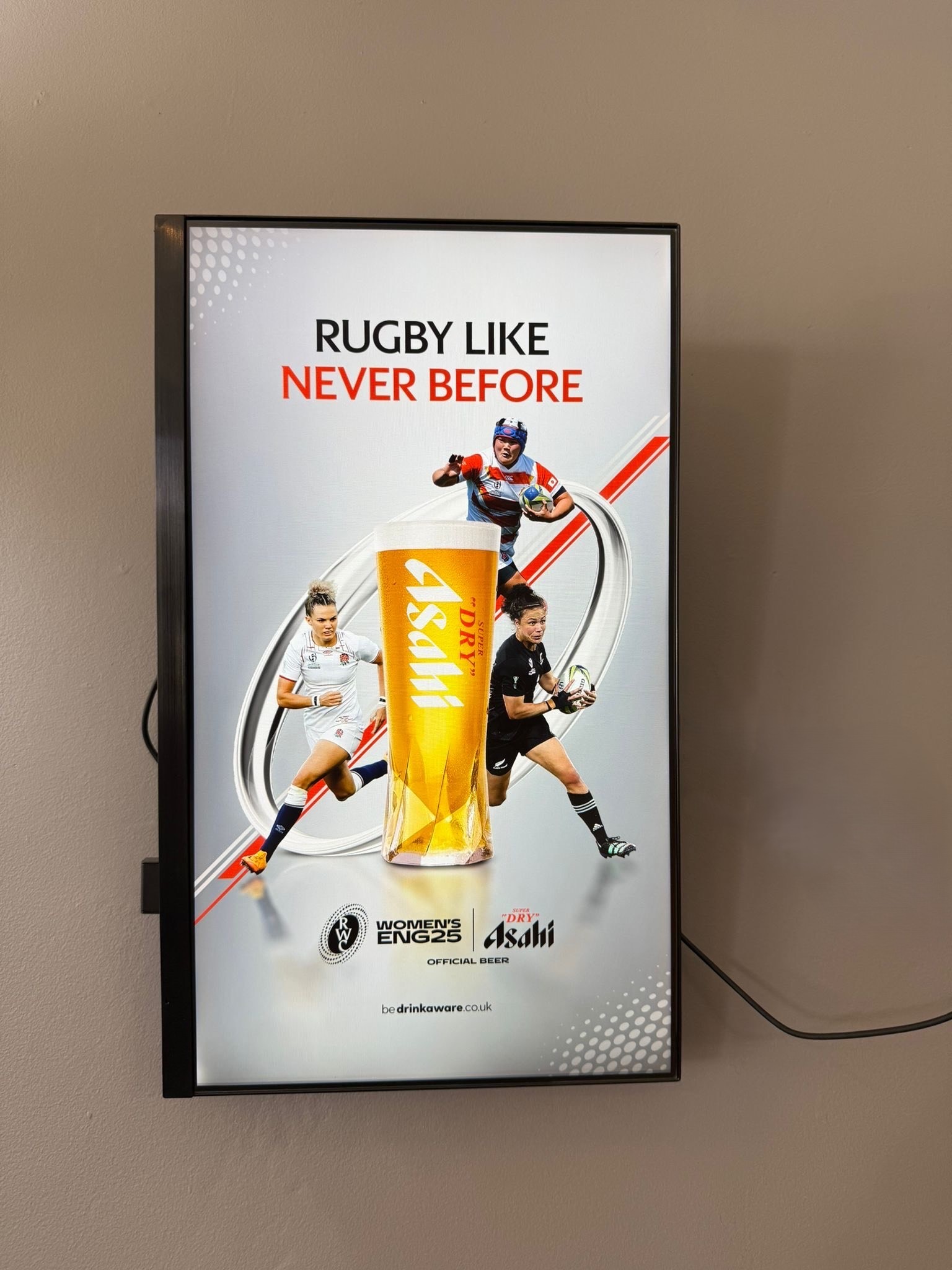 Close-up of a wall-mounted digital screen playing Asahi's 'Rugby Like Never Before' campaign creative featuring international women’s rugby players.