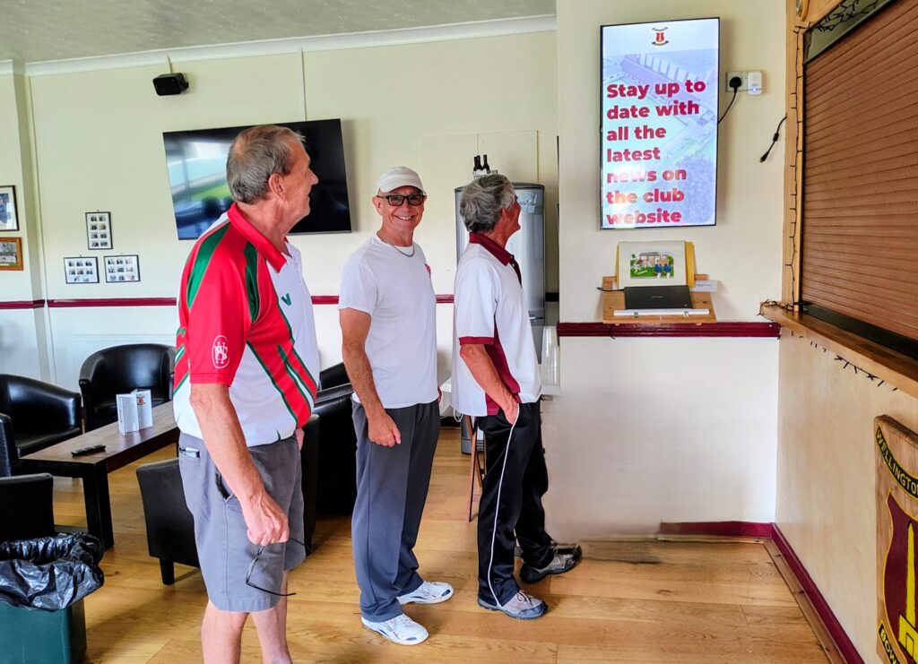 Three bowls club members looking at a digital screen showing club news.