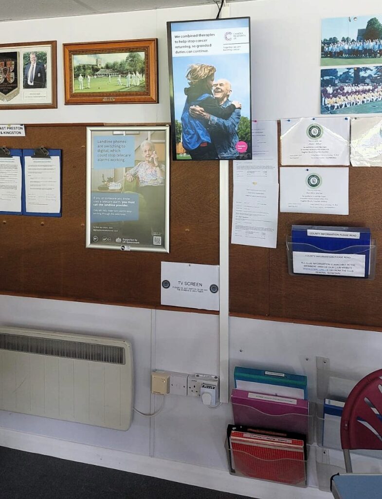 Cancer Research UK advert displayed on a portrait digital screen inside a bowls clubhouse.
