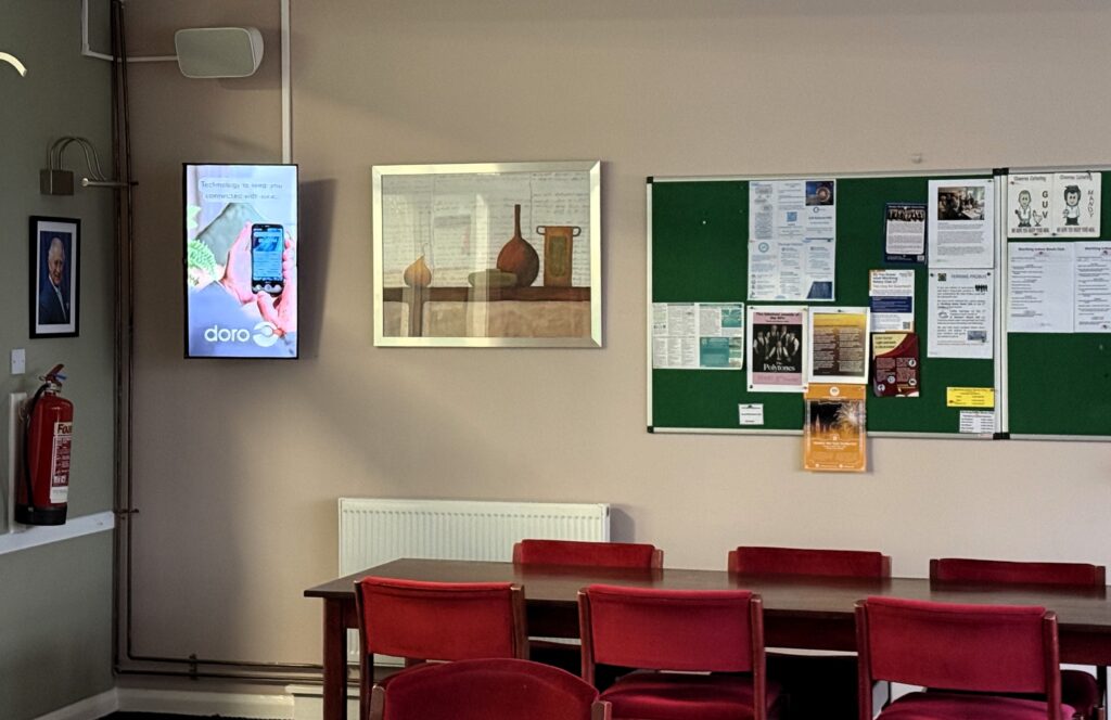 Doro mobile phone advert displayed on a portrait digital screen in a bowls clubhouse social area.