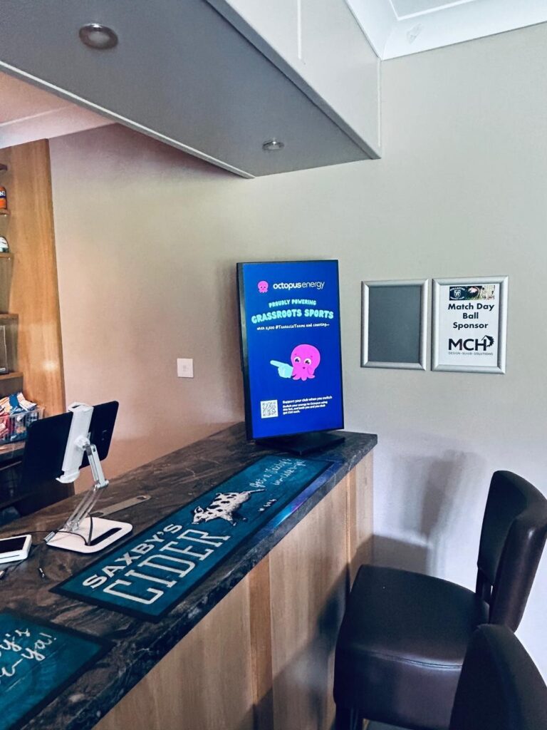 Octopus Energy campaign displayed on a freestanding portrait digital screen beside a grassroots sports club bar.