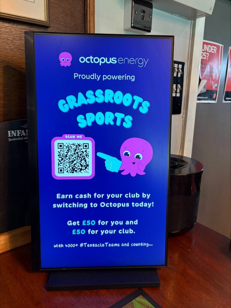 Close-up of an Octopus Energy grassroots sports campaign on a portrait digital screen inside a club venue.