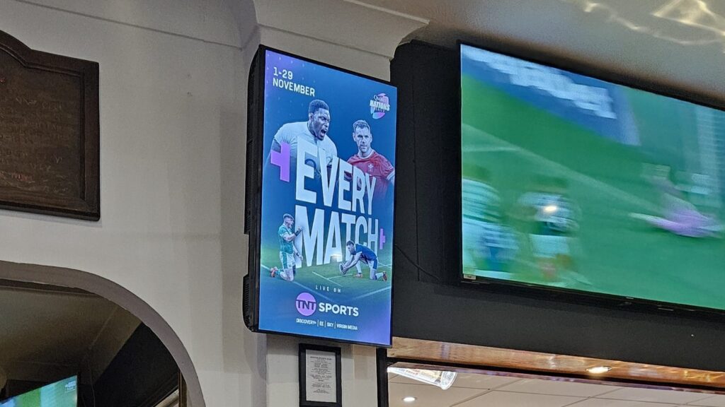 TNT Sports campaign on a portrait screen beside live rugby on a clubhouse television