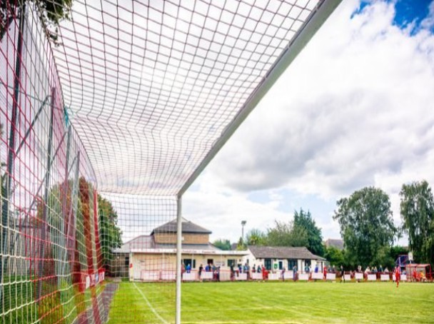 View through a football goal net across Bosham Football Club pitch towards the clubhouse