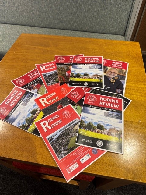 A collection of Bosham FC Robins Review match programmes on a clubhouse table
