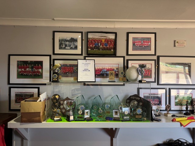 Bosham Football Club trophy cabinet surrounded by framed historic team photographs