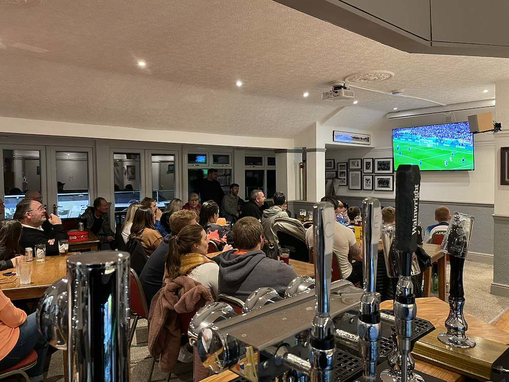 Busy Stone SP Cricket Club clubhouse bar with members watching football on television