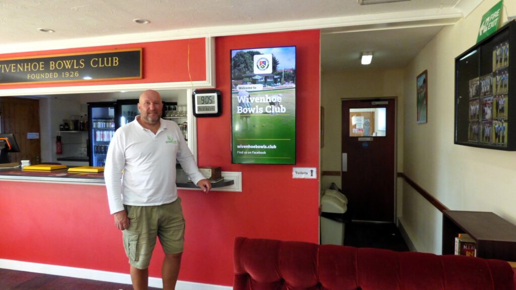 Mat Court standing beside Wivenhoe Bowls Club welcome content on the club’s new Grassroot Media digital screen